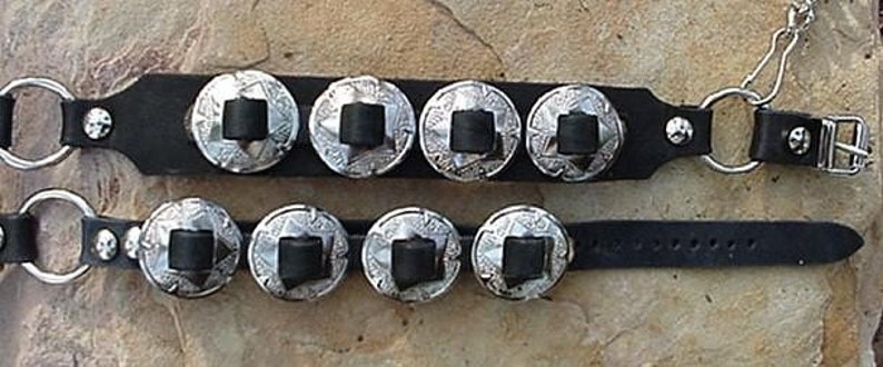 Puede incluir: Dos pulseras de cuero negro con cascabeles plateados. Cada pulsera tiene cinco cascabeles con un dise&ntilde;o en relieve.