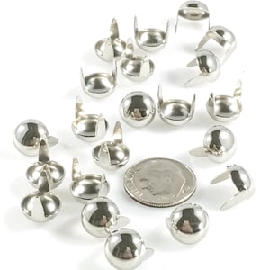 May include: A close-up of a group of silver metal dome-shaped studs with two prongs on the back. The studs are arranged in a circle around a US dime coin for size reference.