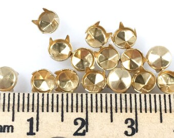 May include: A close-up of 14 gold-toned metal studs with a pointed top and a flat, faceted base. The studs are arranged in a pile and measured against a ruler, showing they are approximately 1/2 inch in diameter.