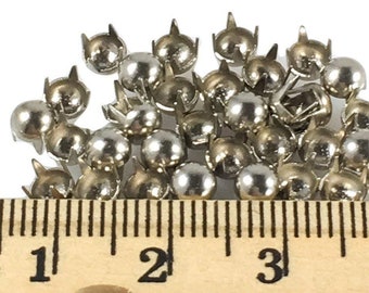 May include: A close-up of a pile of silver metal studs with a ruler showing 4 inches. The studs have a round head with a pointed tip.