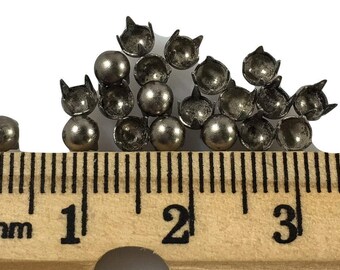 May include: A close-up of a pile of silver metal nailheads with a ruler showing they are about 1/4 inch in diameter.