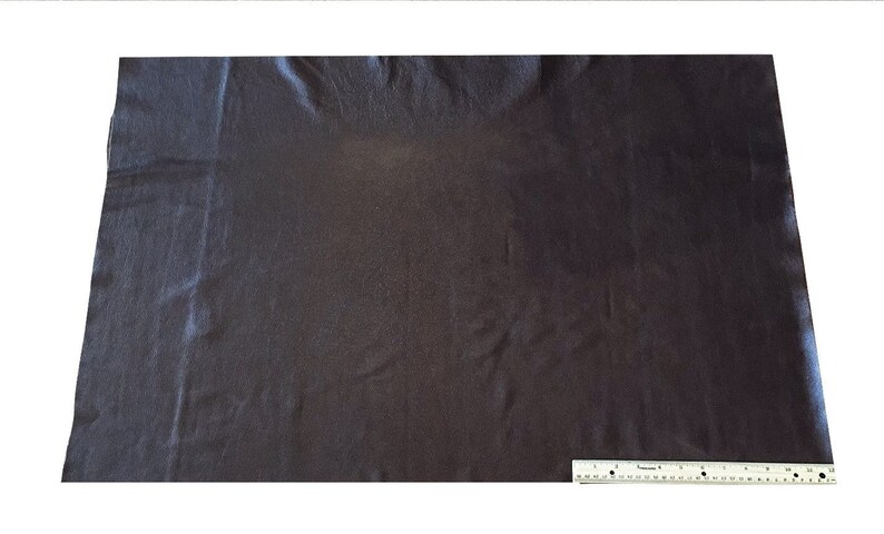 May include: A dark gray fabric swatch with a smooth, slightly textured surface. The fabric is laid flat on a white surface with a ruler for scale.