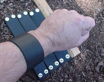 May include: A black leather bracelet with silver snaps. The bracelet is worn on a person's wrist.