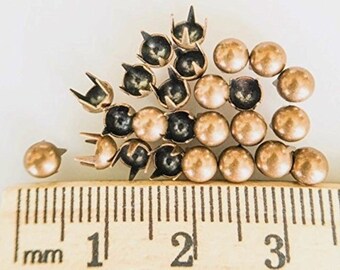 May include: A close-up of a group of 20 gold-toned metal studs with a black center. The studs are arranged in a random pattern and are measured against a ruler.