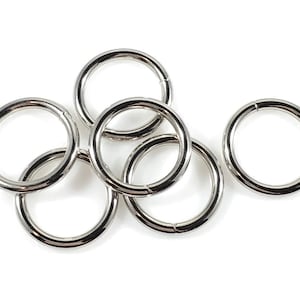 Puede incluir: Seis anillos de metal plateado, algunos superpuestos, sobre un fondo blanco.