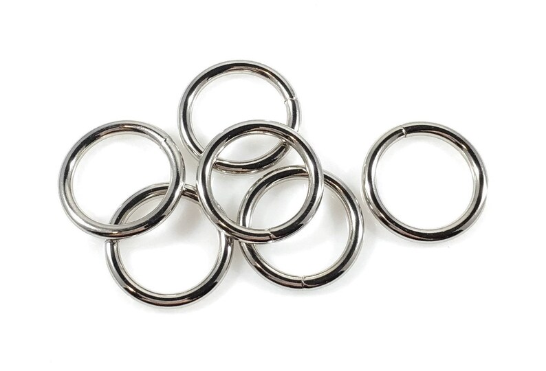 Puede incluir: Seis anillos de metal plateado, algunos superpuestos, sobre un fondo blanco.