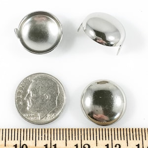 Puede incluir: Tres tachuelas de muebles de metal plateado, cada una con una cabeza redonda y tres puntas. Las tachuelas se muestran junto a una moneda de diez c&eacute;ntimos de euro y una regla, para la escala.