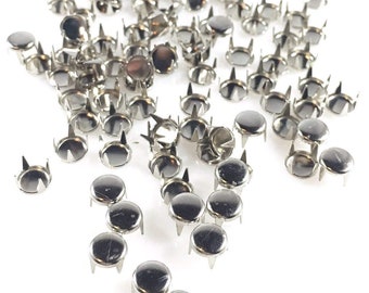 May include: A scattering of silver-toned metal studs with three prongs each. The studs are round and have a smooth, shiny finish.