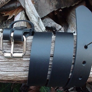 May include: A black leather belt with a silver buckle. The belt is folded and laid on a piece of wood.