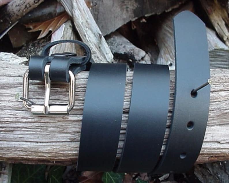 May include: A black leather belt with a silver buckle. The belt is folded and laid on a piece of wood.