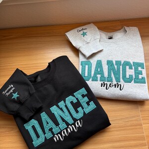 May include: Two sweatshirts, one black and one gray, with teal glitter lettering. The black sweatshirt says "DANCE mama" and the gray one says "DANCE mom". Both have a name and star on the sleeve.