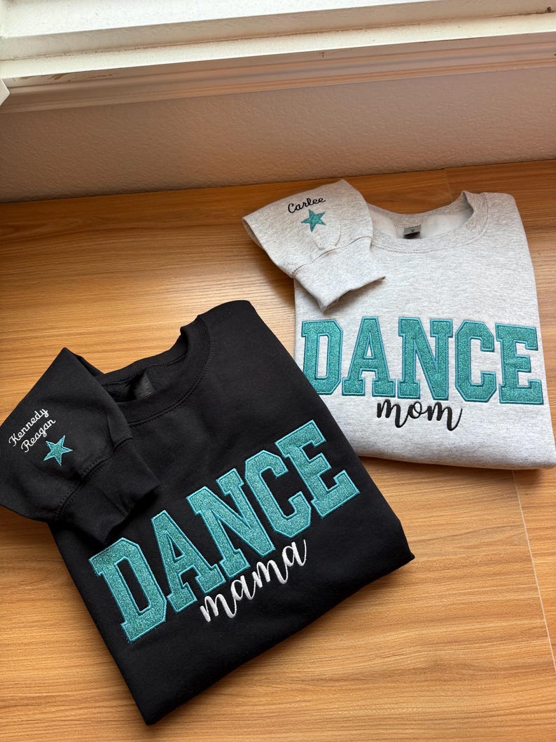 May include: Two sweatshirts, one black and one gray, with teal glitter lettering. The black sweatshirt says "DANCE mama" and the gray one says "DANCE mom". Both have a name and star on the sleeve.