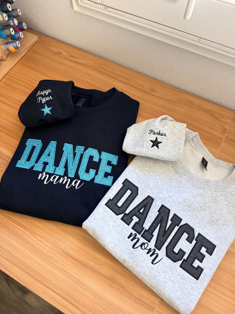 May include: Two sweatshirts and two matching beanies. One navy blue sweatshirt with "DANCE mama" in turquoise lettering and a matching beanie with "Aspyn Pyper" and a star. The other is gray with "DANCE mom" in black lettering and a matching beanie with "Parker" and a star.