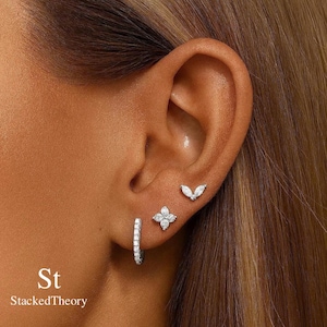 Puede incluir: Primer plano de una oreja adornada con tres juegos de pendientes. Un aro pequeño con piedras transparentes, un diseño de flor de cuatro pétalos y un pendiente en forma de marquesa. El texto "St StackedTheory" está en la esquina inferior izquierda.