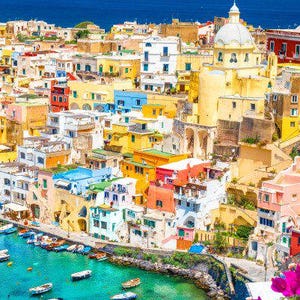 May include: A colorful cityscape with a variety of buildings, including a large church with a dome. The buildings are clustered together on a hillside overlooking a turquoise blue body of water. Boats are docked in the water.