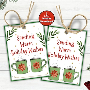 Puede incluir: Dos etiquetas rectangulares para regalo con el texto "Sending Warm Holiday Wishes" en rojo. Cada etiqueta presenta dos tazas verdes con diseños de copos de nieve rojos. Las etiquetas tienen un borde verde y están atadas con hilo.