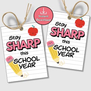 Puede incluir: Dos etiquetas blancas con el texto "Stay SHARP this SCHOOL YEAR" en rosa y negro. Cada etiqueta presenta una manzana roja y un lápiz amarillo con una goma de borrar rosa. Las etiquetas están unidas con hilo.