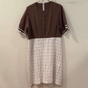 May include: A brown and white dress with a checkered pattern on the lower half and a solid brown top. The dress has short sleeves with white stripes at the cuffs and a zipper closure.