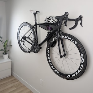 May include: A black bicycle with a white helmet hanging on a white wall. The bicycle has black wheels with white lettering that says "VICTORY"