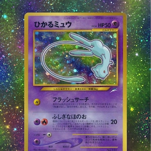 Puede incluir: Una carta coleccionable Pokémon holográfica con el personaje "Hikaru Mew". La tarjeta tiene un borde púrpura con texto japonés y una ilustración de Mew azul claro. La tarjeta también tiene una clasificación HP50.