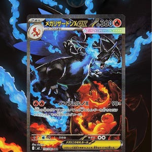 Puede incluir: Carta coleccionable con Mega Charizard X negro y azul. Texto japonés y fondo de fuego. La ilustración muestra una criatura con forma de dragón con llamas.