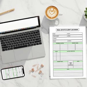May include: A workspace with a laptop, smartphone, and a printed "REAL ESTATE CLIENT LOG BOOK." A cup of coffee, a succulent plant, and a gold pen are also on the white marble surface. Paper clips and wireless earbuds are scattered around.