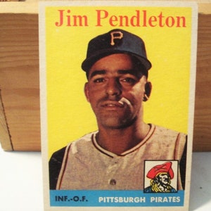 May include: A vintage baseball card featuring Jim Pendleton wearing a dark blue cap with a yellow P and a light-colored jersey. The card has a bright yellow background, a small pirate illustration in the corner, and text reading Jim Pendleton.