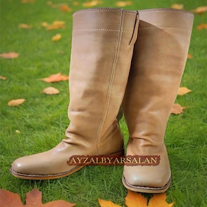 May include: A pair of tan leather knee-high boots with a pointed toe and a slight heel. The boots are made of soft, supple leather and have a classic, timeless design.