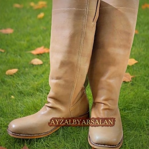 May include: A pair of tan leather knee-high boots with a pointed toe and a slight heel. The boots are made of a soft, supple leather and have a classic, timeless design.