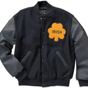 Puede incluir: Chaqueta de béisbol negra con mangas de cuero y un gran parche de fieltro naranja con un trébol y la palabra "IRISH" en la parte delantera.