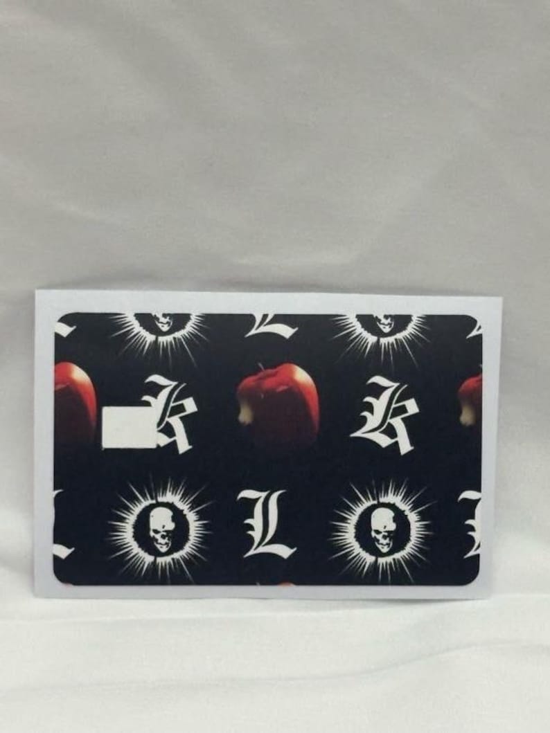 Op de afbeelding: Een rechthoekige sticker met een zwarte achtergrond met een patroon van witte gestileerde letters, schedels en een rode appel. De appel heeft een hap uit. De sticker heeft een witte rand.