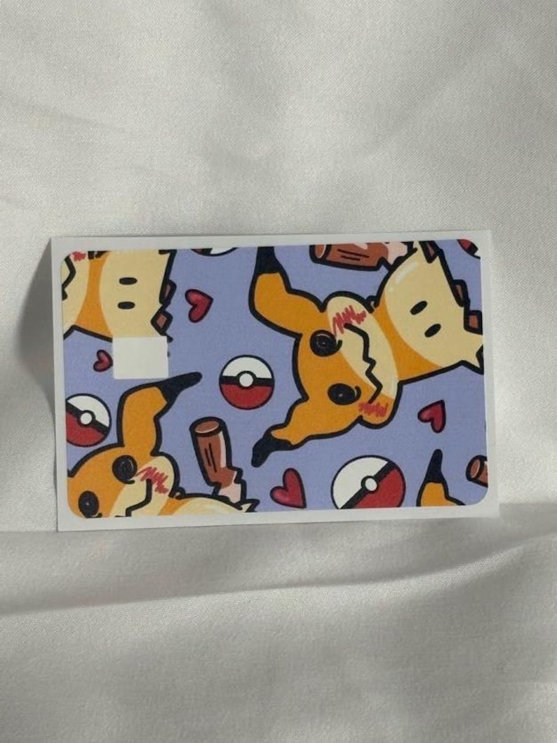 Op de afbeelding: Een rechthoekige sticker met een herhaald patroon van een gele stripfiguur met zwarte accenten, rode harten en rood-witte cirkelvormige ontwerpen op een lichtblauwe achtergrond. De sticker heeft een witte rand.