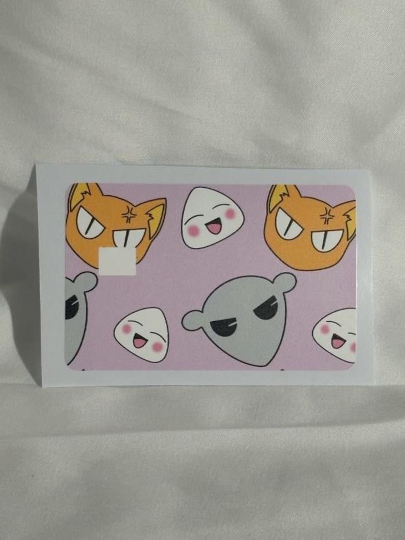 Op de afbeelding: Een rechthoekige sticker met cartoonkarakterontwerpen op een roze achtergrond. De sticker bevat oranje kattengezichten, witte rijstbal-personages en grijze buitenaardse figuren. De sticker is geplaatst tegen een witte achtergrond.