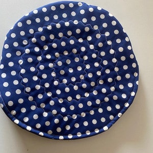 May include: A blue and white polka dot quilted round hot pad. The pad is quilted in a spiral pattern.