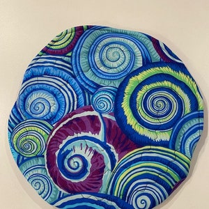 Puede incluir: Un posavasos redondo de tela con un patrón de espiral de azul, verde, morado y blanco. El diseño presenta una variedad de formas espirales.