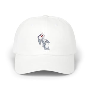 May include: White baseball cap with an embroidered Bugs Bunny design. The cap has a curved peak and a classic six-panel construction. The Bugs Bunny image is in shades of grey, white, and red.