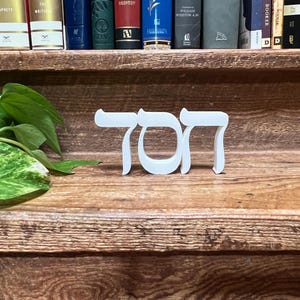 May include: A white three-dimensional Hebrew word sculpture featuring the letters Chet, Vav, and Tav. The freestanding object is crafted with a smooth matte finish and clean edges, displaying the Hebrew characters clearly in a bold, sans-serif style.