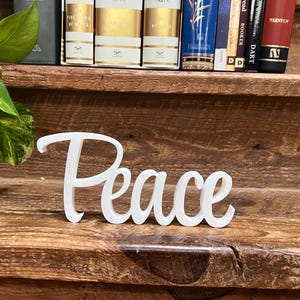 May include: White wooden sign with the word "Peace" in a cursive font.