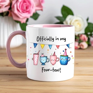 May include: White ceramic mug with a pink interior and handle. The mug features the text "Officially in my Four-teas!" above four cartoon tea cups with party hats. Colorful confetti and a banner with pennants decorate the mug.