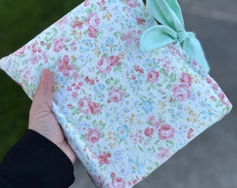 May include: A small, white fabric pouch with a floral print and a light green bow. The pouch is made of a soft, quilted fabric and has a zipper closure.
