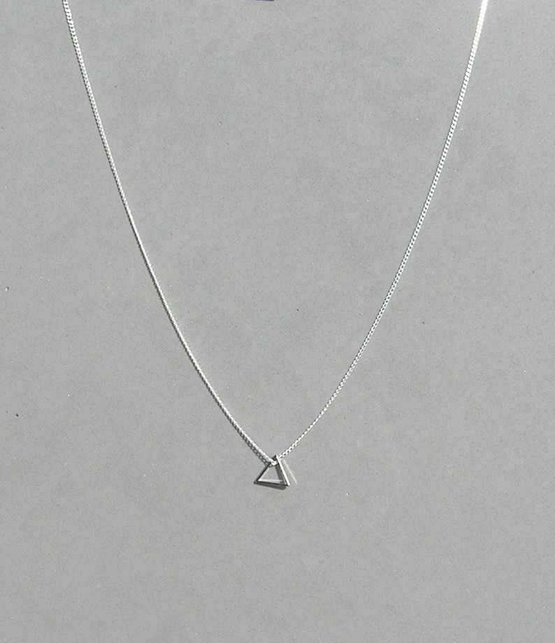 May include: A silver chain necklace with a small, simple triangle pendant.