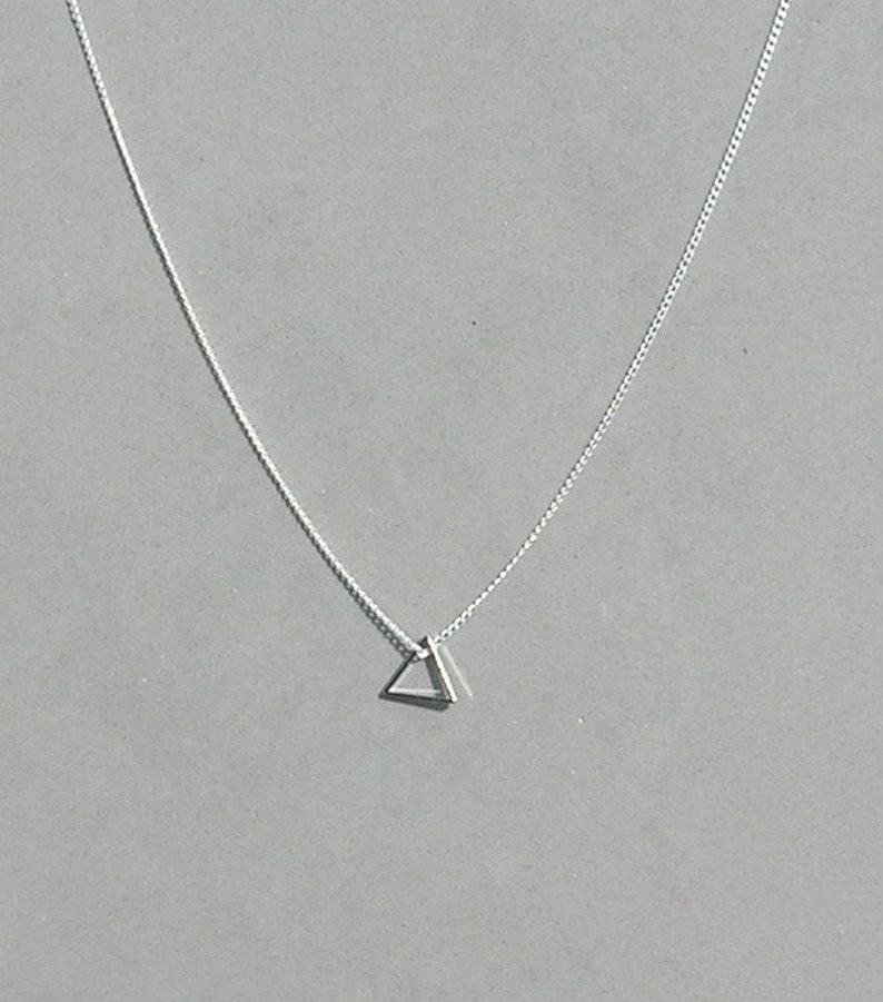 May include: A silver chain necklace with a small, double-layered triangle pendant.