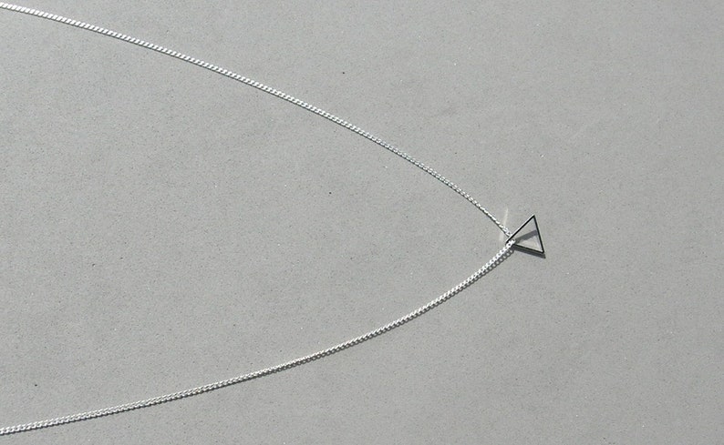 May include: A silver chain necklace with a small, simple triangle pendant.