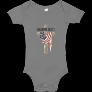 Puede incluir: Body de beb&eacute; gris con un dise&ntilde;o de cruz de madera adornada con una bandera americana. El texto "IN GOD WE TRUST" est&aacute; sobre la cruz. El body tiene mangas cortas y cierres de presi&oacute;n.