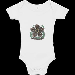 May include: White baby onesie featuring a Demogorgon flower graphic. The graphic is brown, green, and tan. The onesie has short sleeves and snaps at the bottom. A cute and unique baby outfit.
