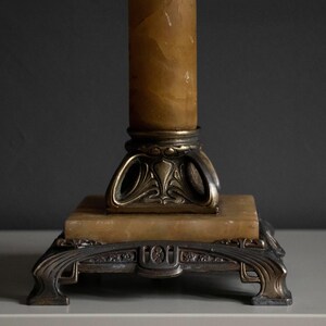 May include: A vintage lamp base with a decorative, ornate design. The base is made of metal and features a column of alabaster. The base is finished in a gold tone.