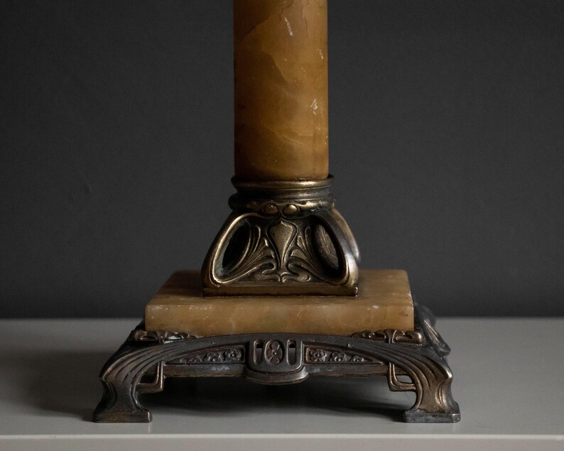 May include: A vintage lamp base with a decorative, ornate design. The base is made of metal and features a column of alabaster. The base is finished in a gold tone.