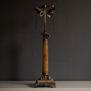May include: A vintage table lamp with a white alabaster column and a brass base. The lamp has two sockets and a decorative finial.