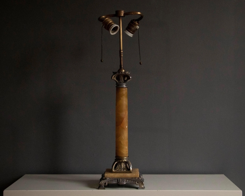 May include: A vintage table lamp with a white alabaster column and a brass base. The lamp has two sockets and a decorative finial.