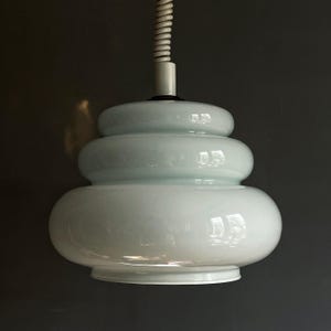 Puede incluir: Una lámpara colgante blanca con una pantalla de vidrio redonda en capas. La pantalla está hecha de múltiples capas de vidrio, creando un aspecto único y moderno.